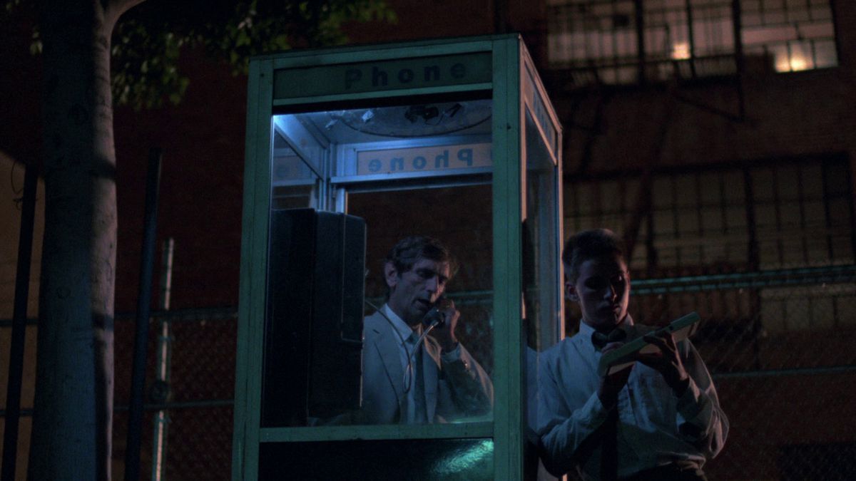 Harry Dean Stanton takes a call in a phone booth while Emilio Estevez waits outside in Repo Man