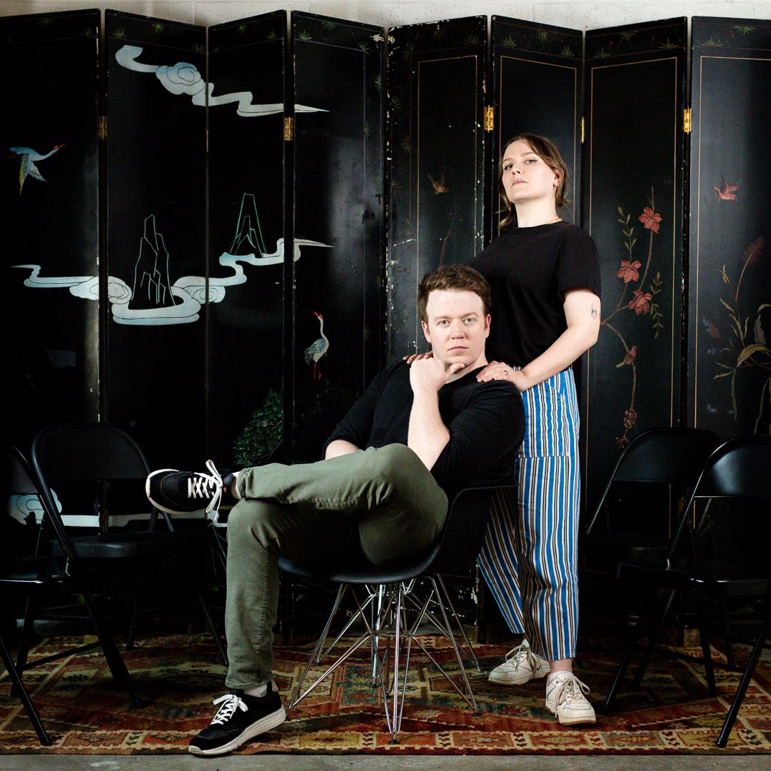 Promo image of Bigger, with Brennan Lee Mulligan and Izzy Roland making silly poses in front of a decorated screen