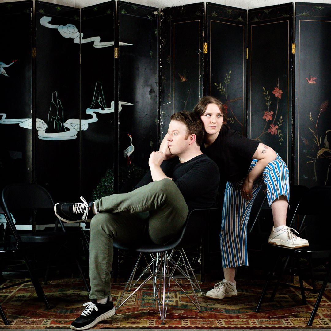 Promo image of Bigger, with Brennan Lee Mulligan and Izzy Roland making silly poses in front of a decorated screen