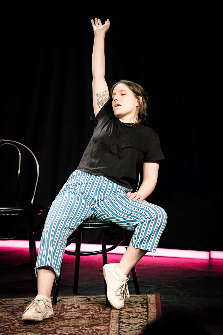 Izzy Roland, eyes closed, holds her arm up while slouching in a chair in Bigger