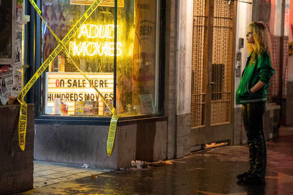 Maxine (Mia Goth) stands outside a store with a bright neon-yellow “adult movies” sign and police “crime scene do not cross” tape strung up in an X across the door in Ti West’s Maxxxine