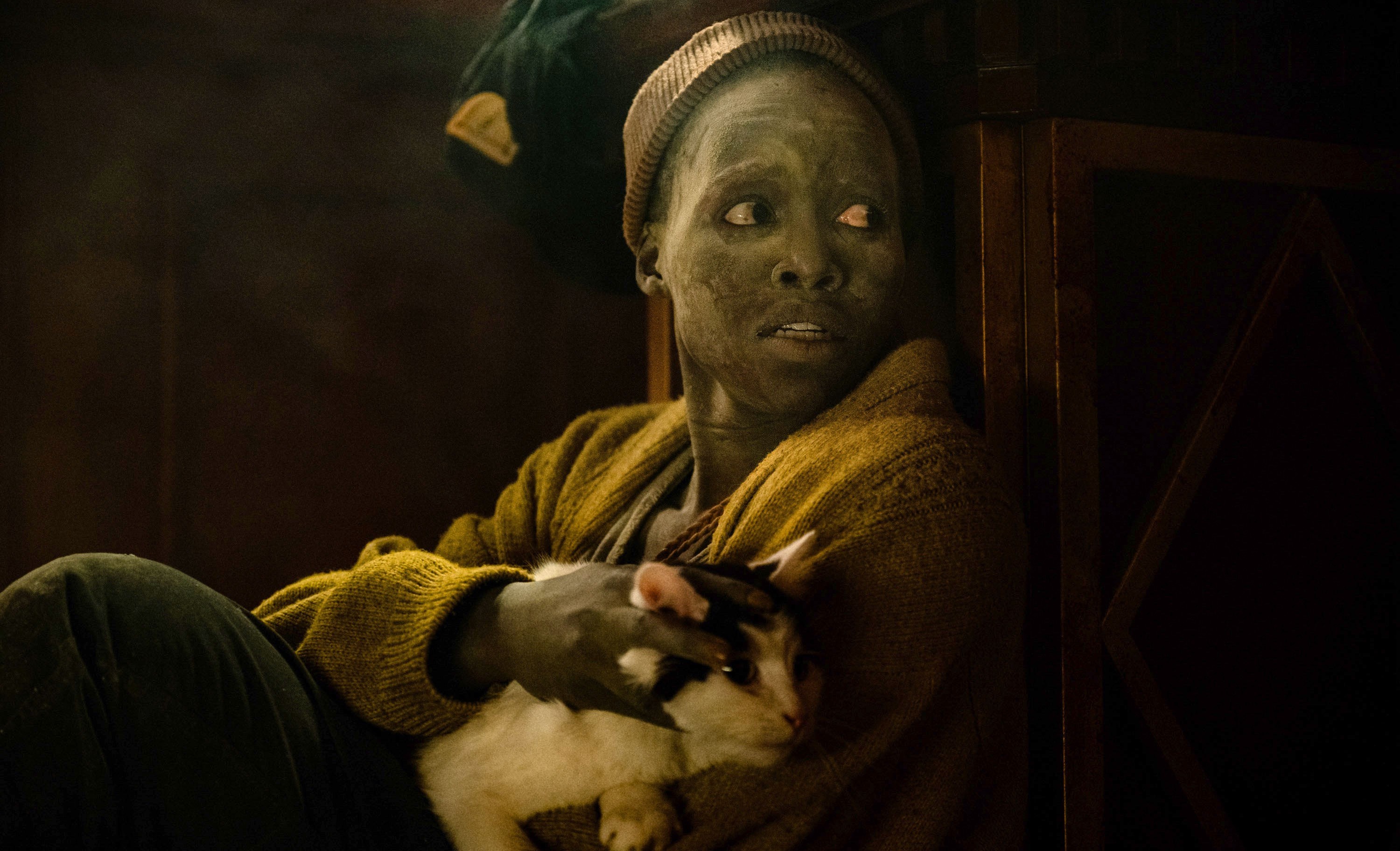 Sam (Lupita Nyong’o) sits fearfully in a dark space, covered with dust, her cat Frodo in her lap, in Michael Sarnoski’s A Quiet Place: Day One