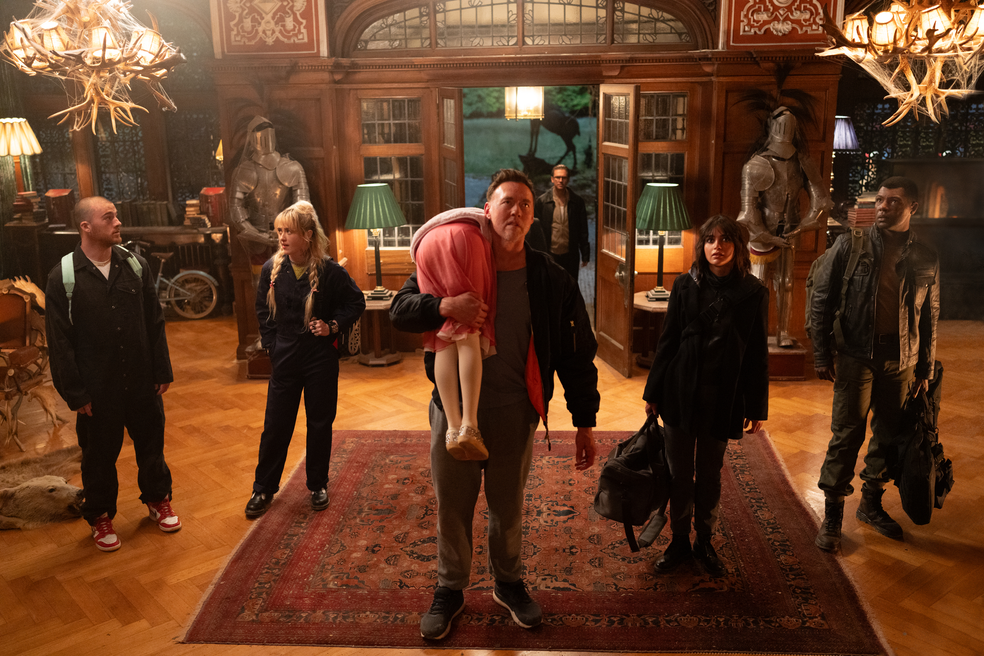 Kevin Durand, Alisha Weir, Kathryn Newton, Dan Stevens, Melissa Barrera, Angus Cloud, and William Catlett stand in the lobby of a fancy mansion in Abigail