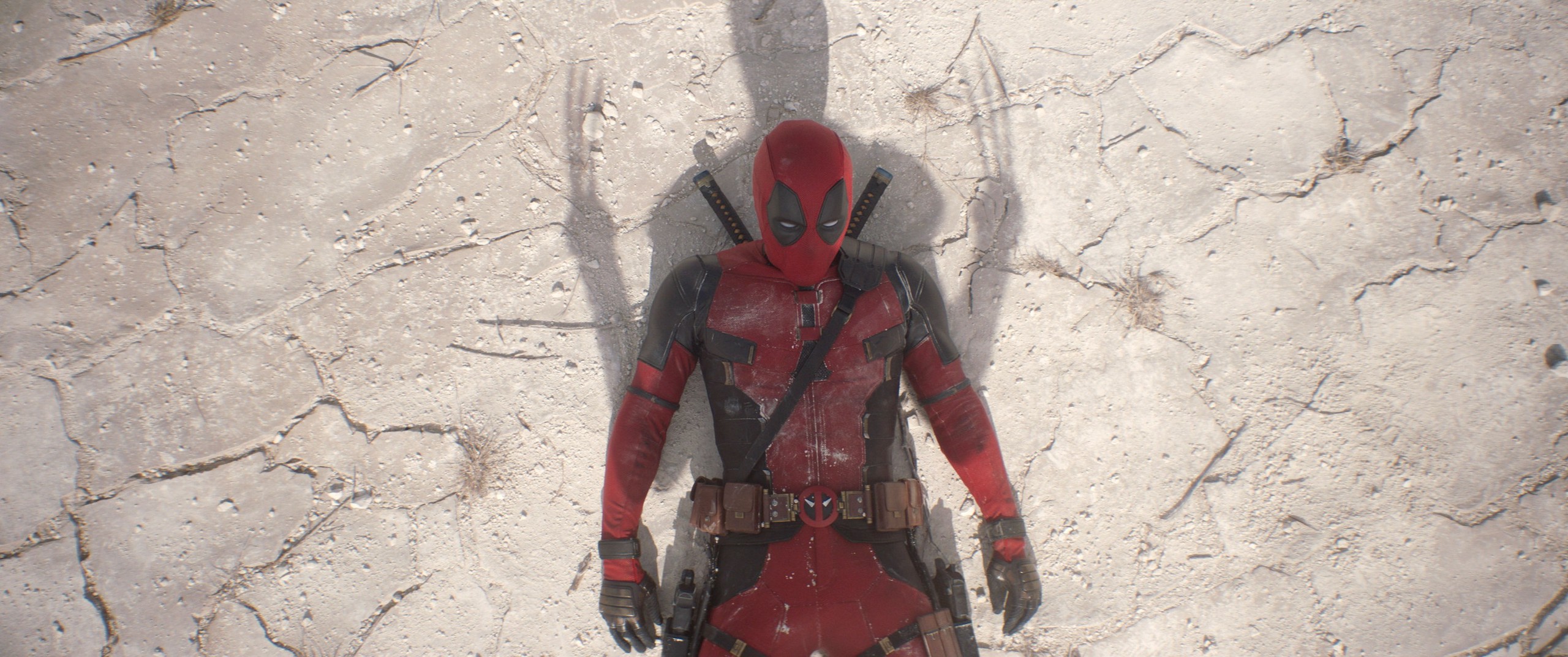 Deadpool (Ryan Reynolds) lies on his back in the sand with Wolverine’s shadow superimposed over him, claws out, in Deadpool & Wolverine