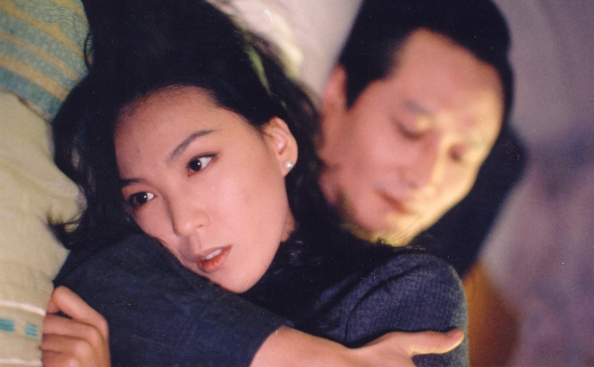 A woman and a man embracing on a bed in Green Fish.