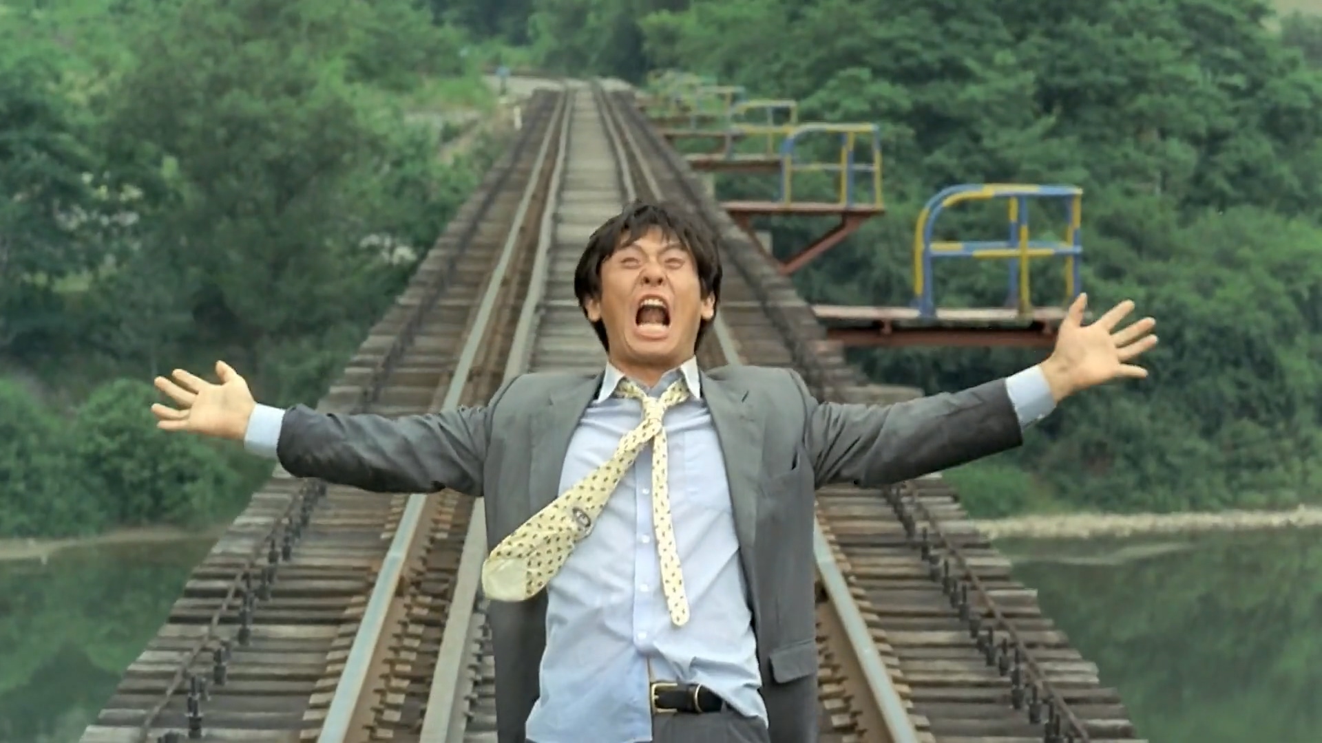 A man in a suit standing in the middle of train tracks overlooking a bridge in Peppermint Candy.