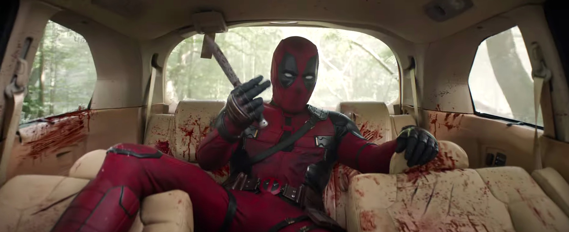 Deadpool taunts unseen adversaries as he sits bleeding in the back of a car while holding a knife in Deadpool &amp; Wolverine