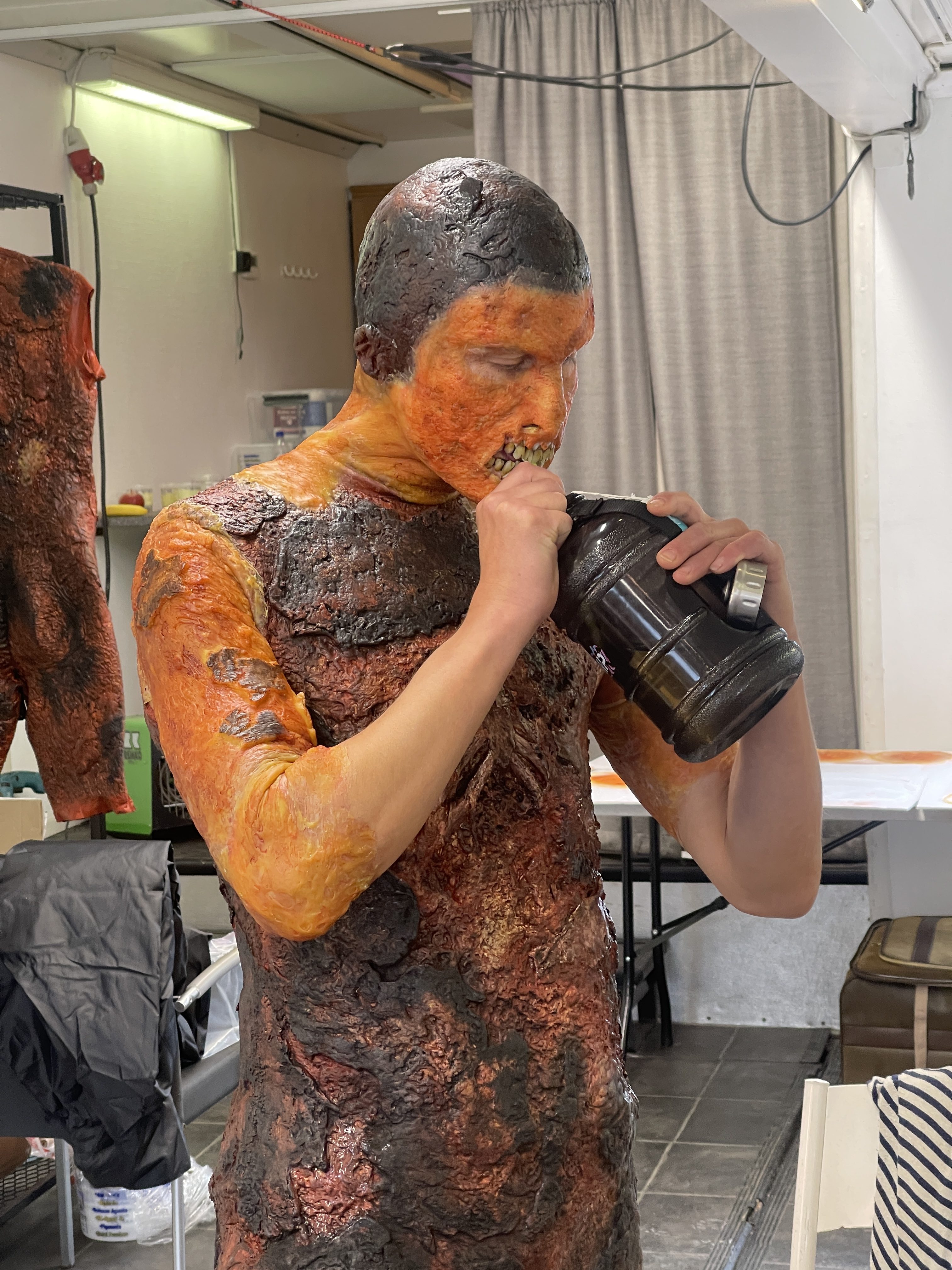 An actor in partially applied Burned One makeup behind the scenes, drinking from a water bottle