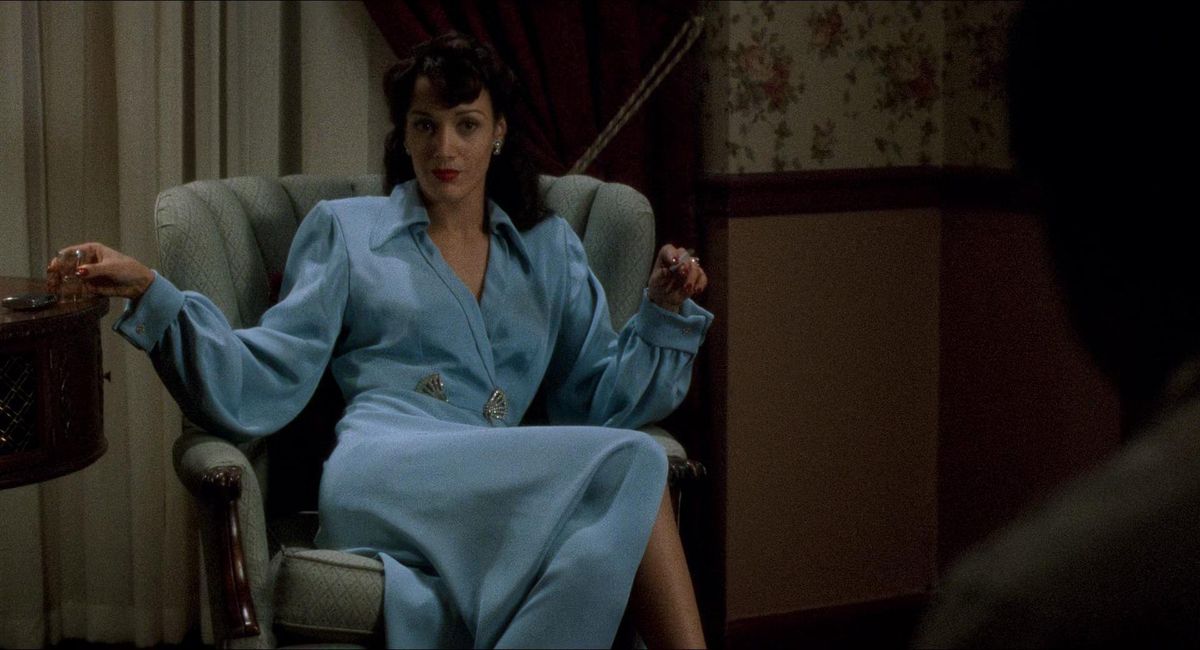 Jennifer Beals wears a light blue dress while sitting in a chair in Devil in a Blue Dress (that’s the devil in a blue dress, your date says)
