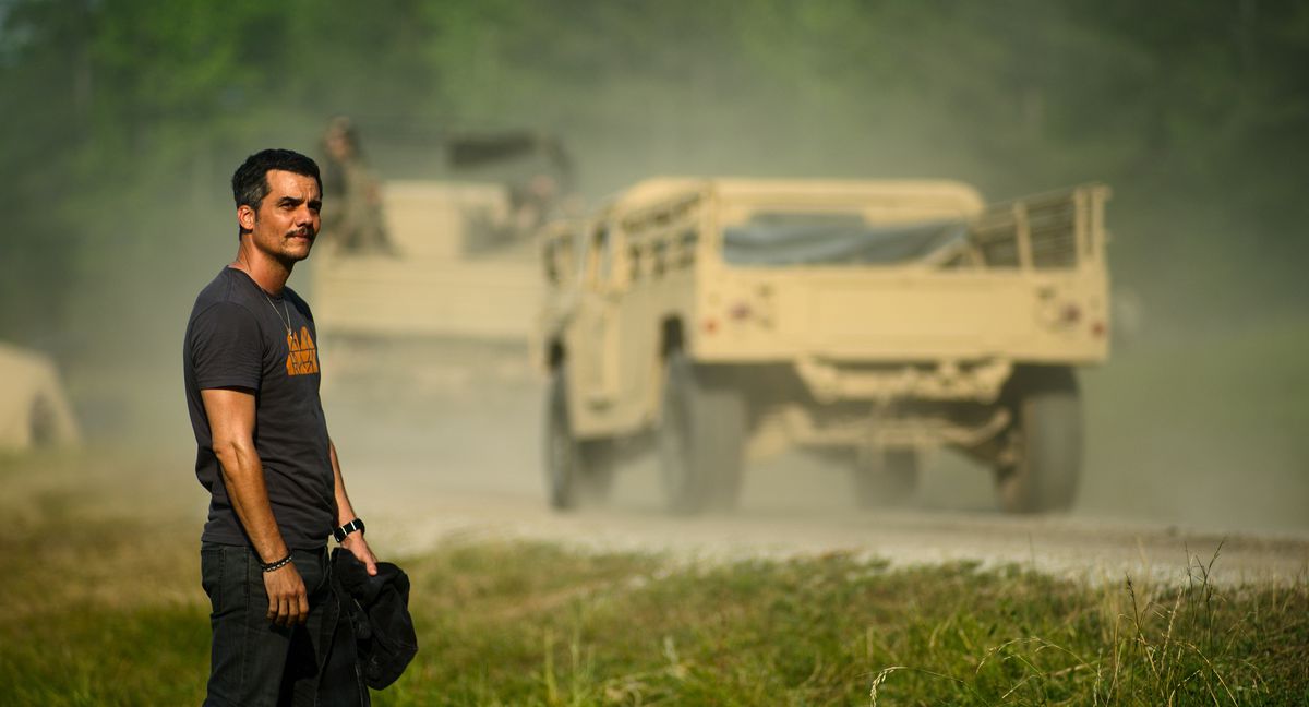 War correspondent Joel (Wagner Moura) stands in the grass by the side of a dusty road as huge military vehicles drive by in Alex Garland’s Civil War