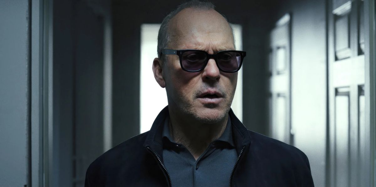 A man wearing sunglasses stands in a darkened doorway.