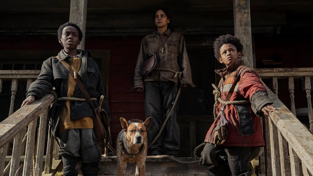 A woman (Halle Berry) standing on a porch next to two young boys with rope tied around their waists connected to a dog in Never Let Go.