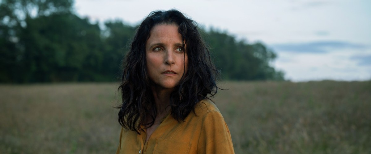 A close-up of a woman in a yellow shirt with dark long hair standing in a field in Tuesday.