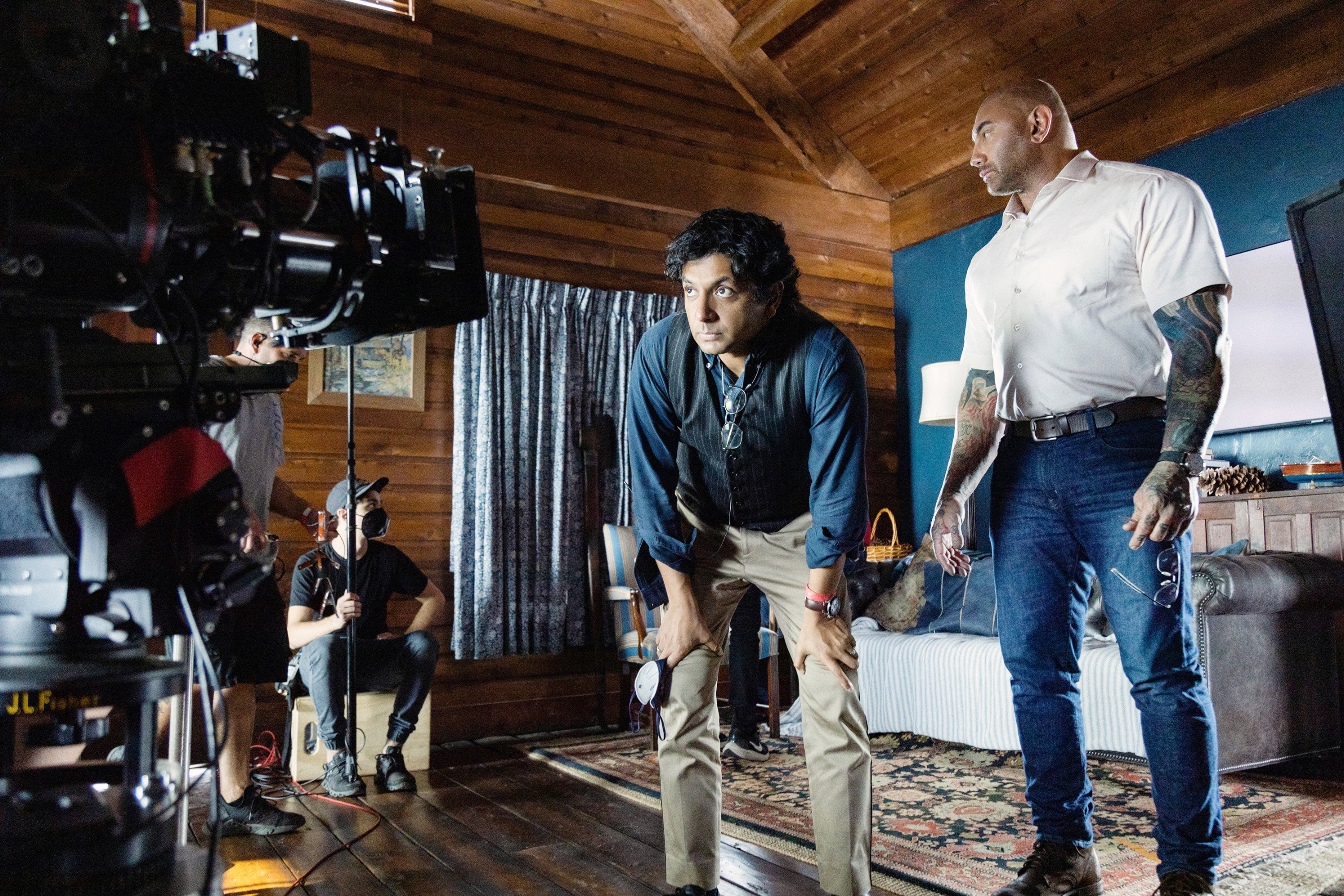 M. Night Shyamalan standing next to a camera on set with Dave Bautista for Knock at the Cabin 