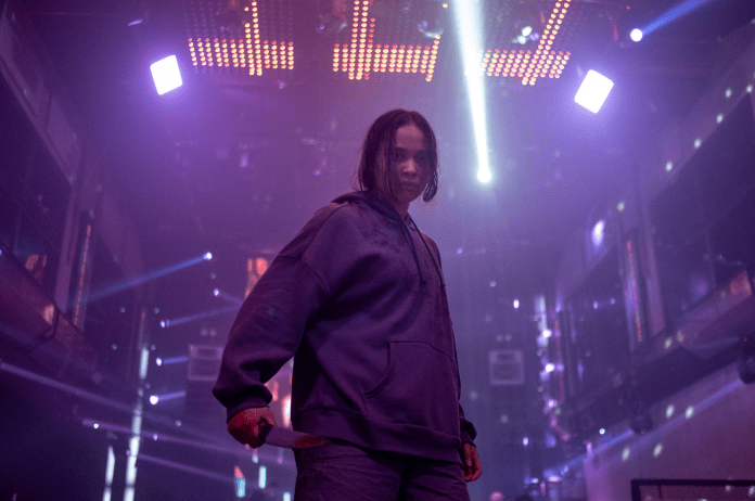 Aurora Ribero, wearing a purple hoodie, holds a bloody knife in what looks like a dance club in The Shadow Strays