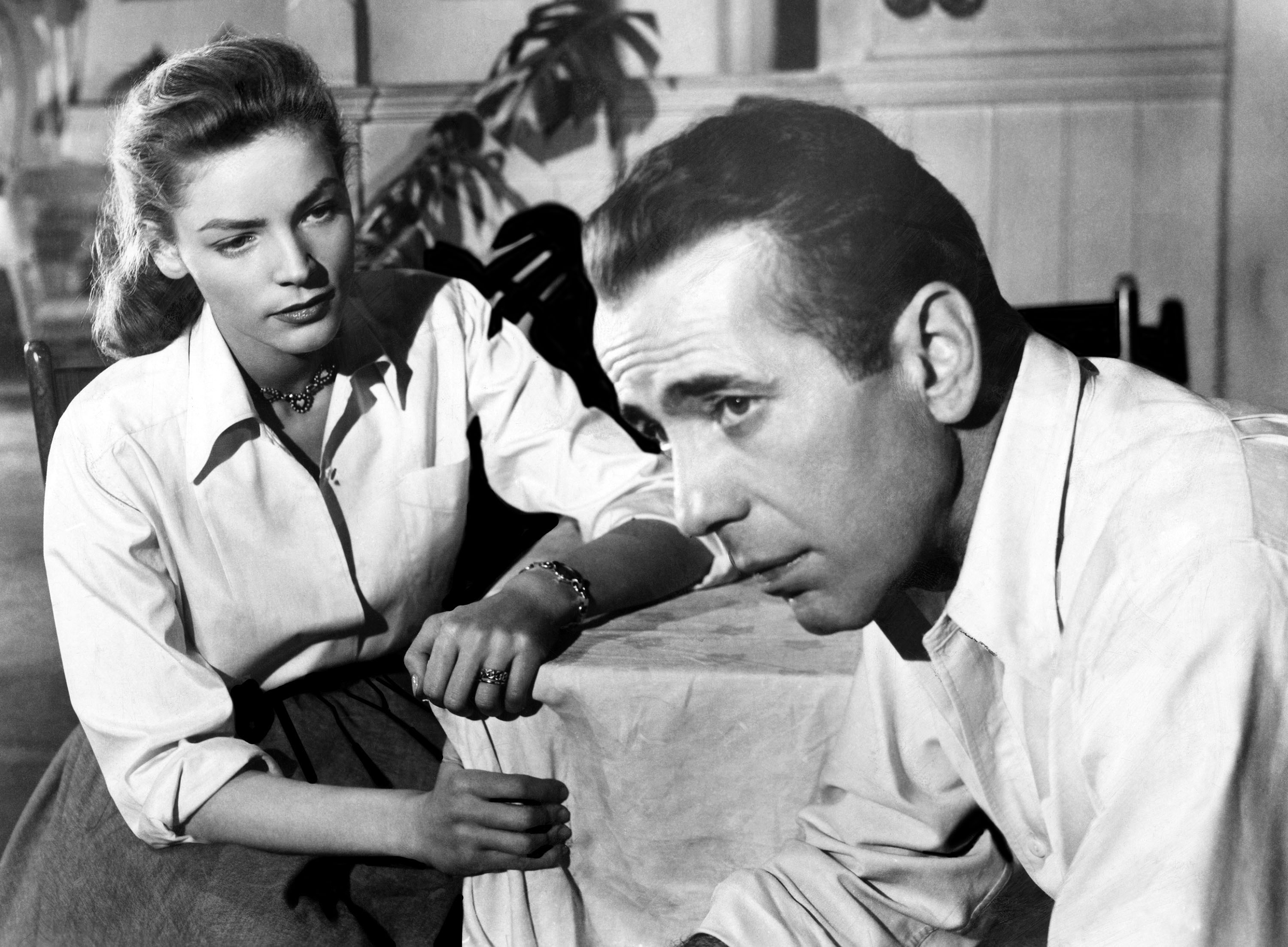 Humphrey Bogart and Lauren Bacall, both looking beautiful and dressed for Florida weather, sit at a table in Key Largo