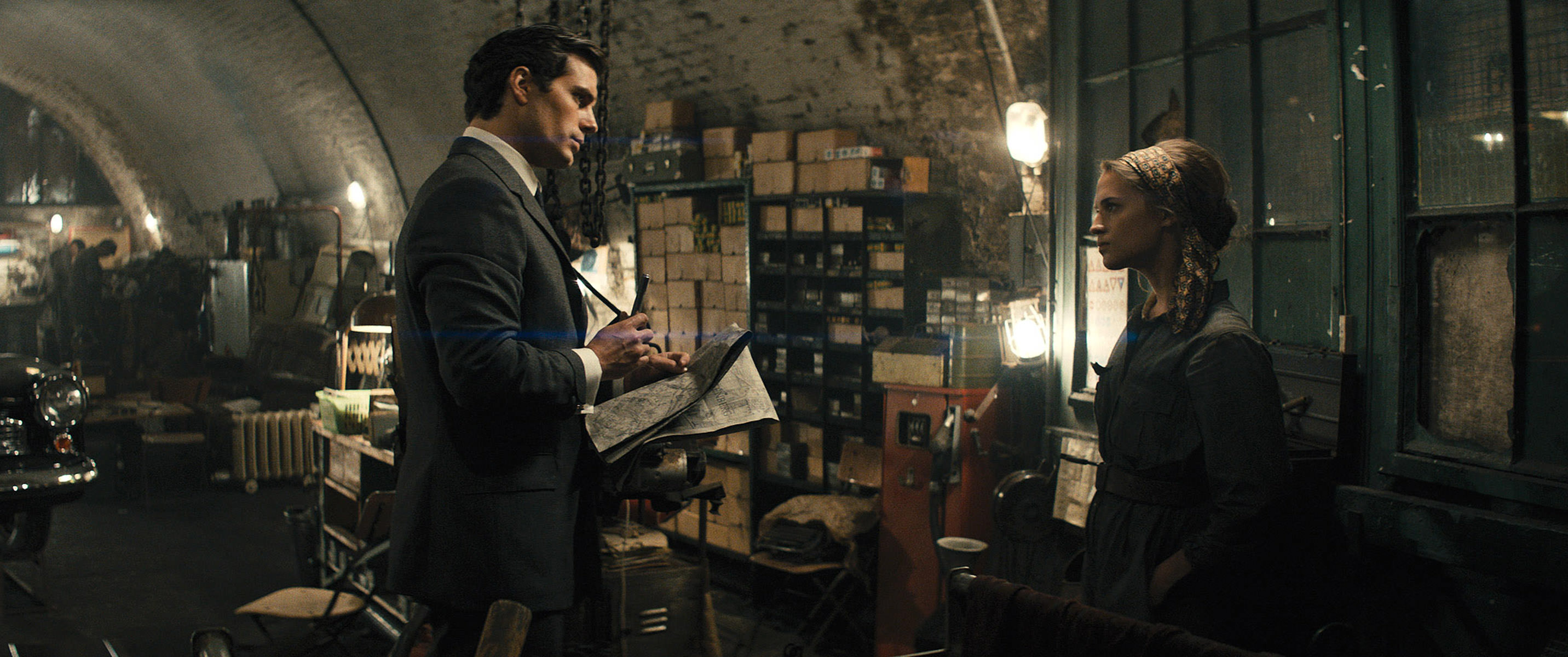 A dapper Henry Cavill confronts a grubby Alicia Vikander in a cluttered safehouse in The Man From UNCLE.