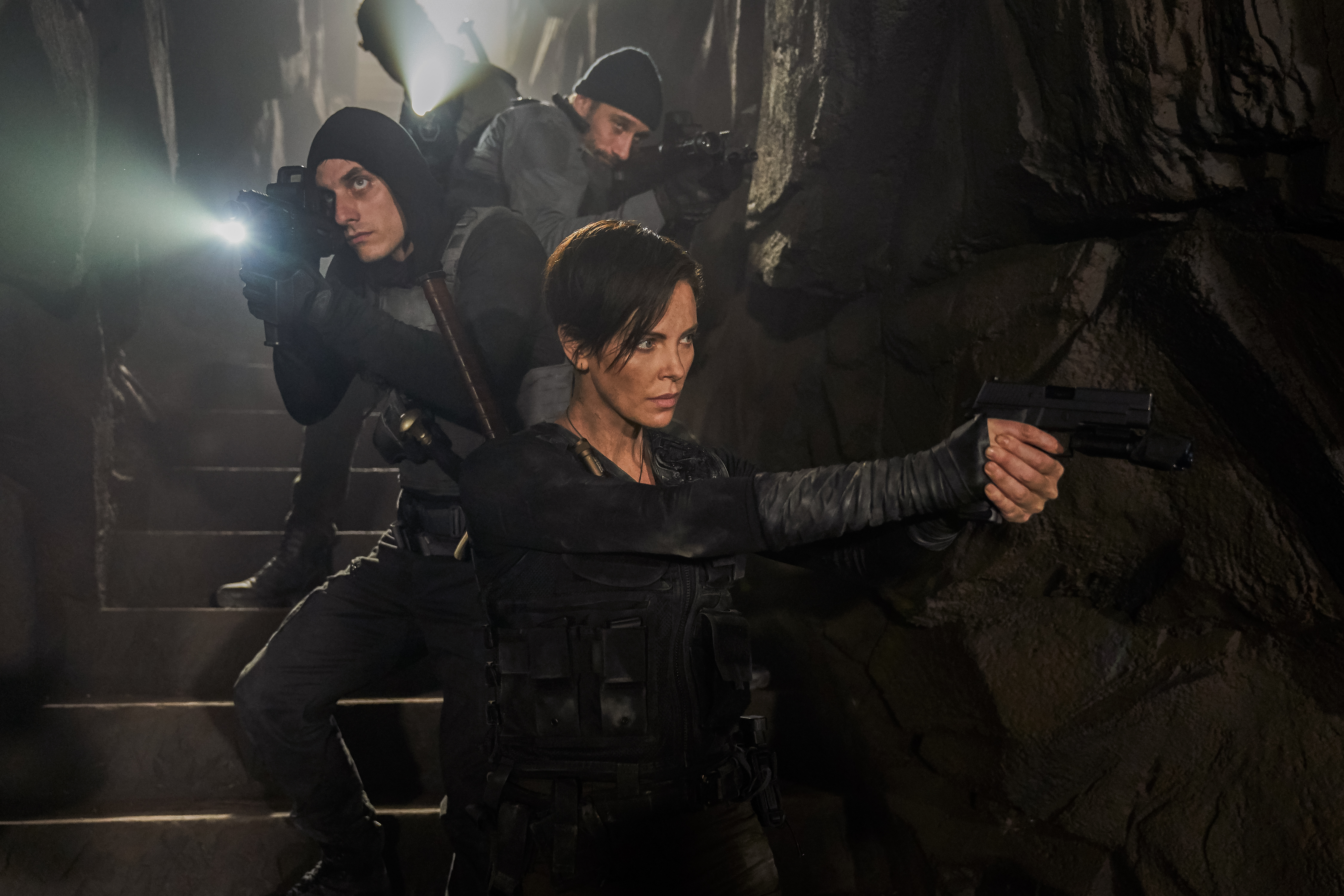 Charlize Theron leads her team down into a dark underground area in The Old Guard.