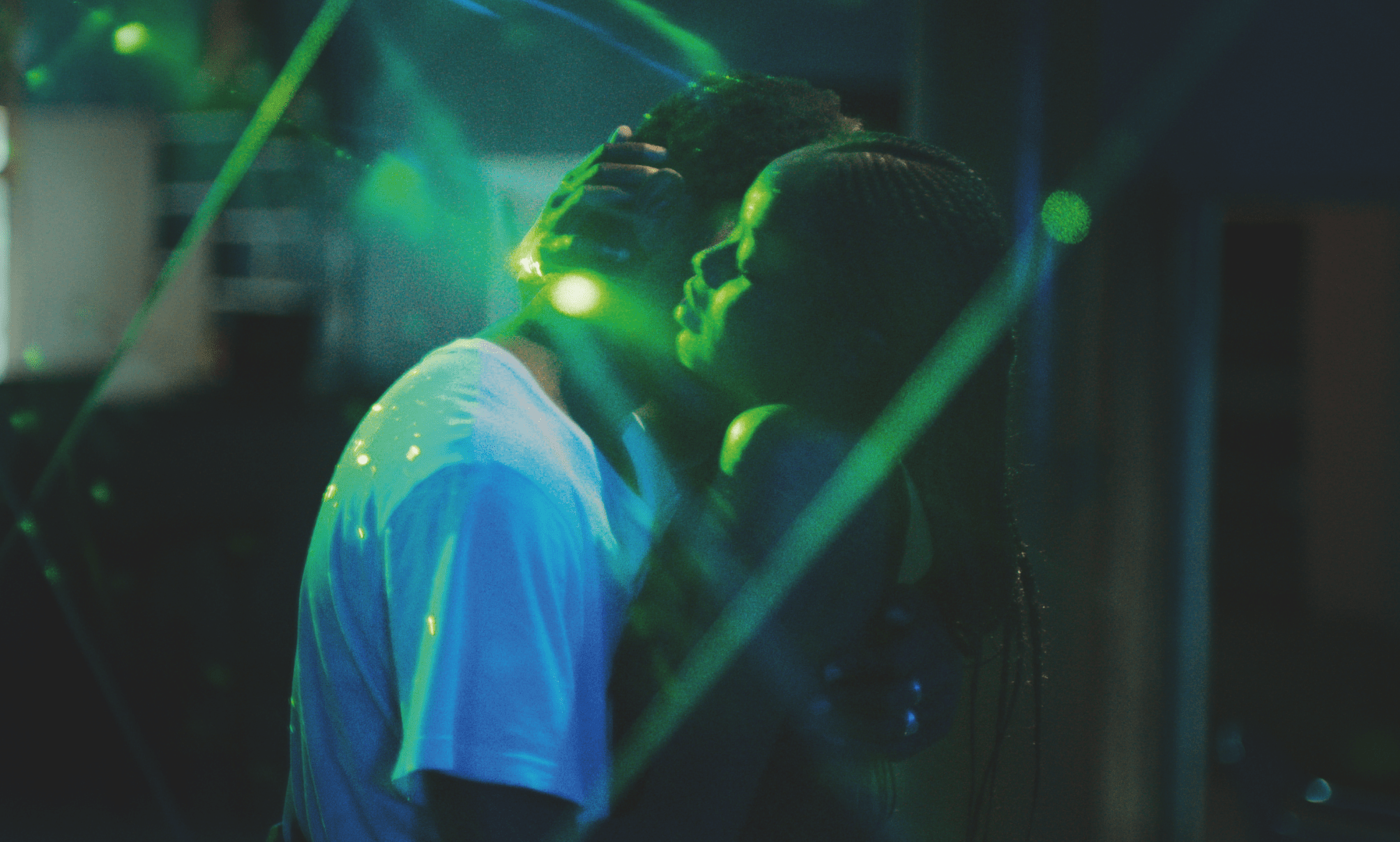 Two figures hold each other close on a dance floor, as neon green lights bounce off of them, in Atlantics