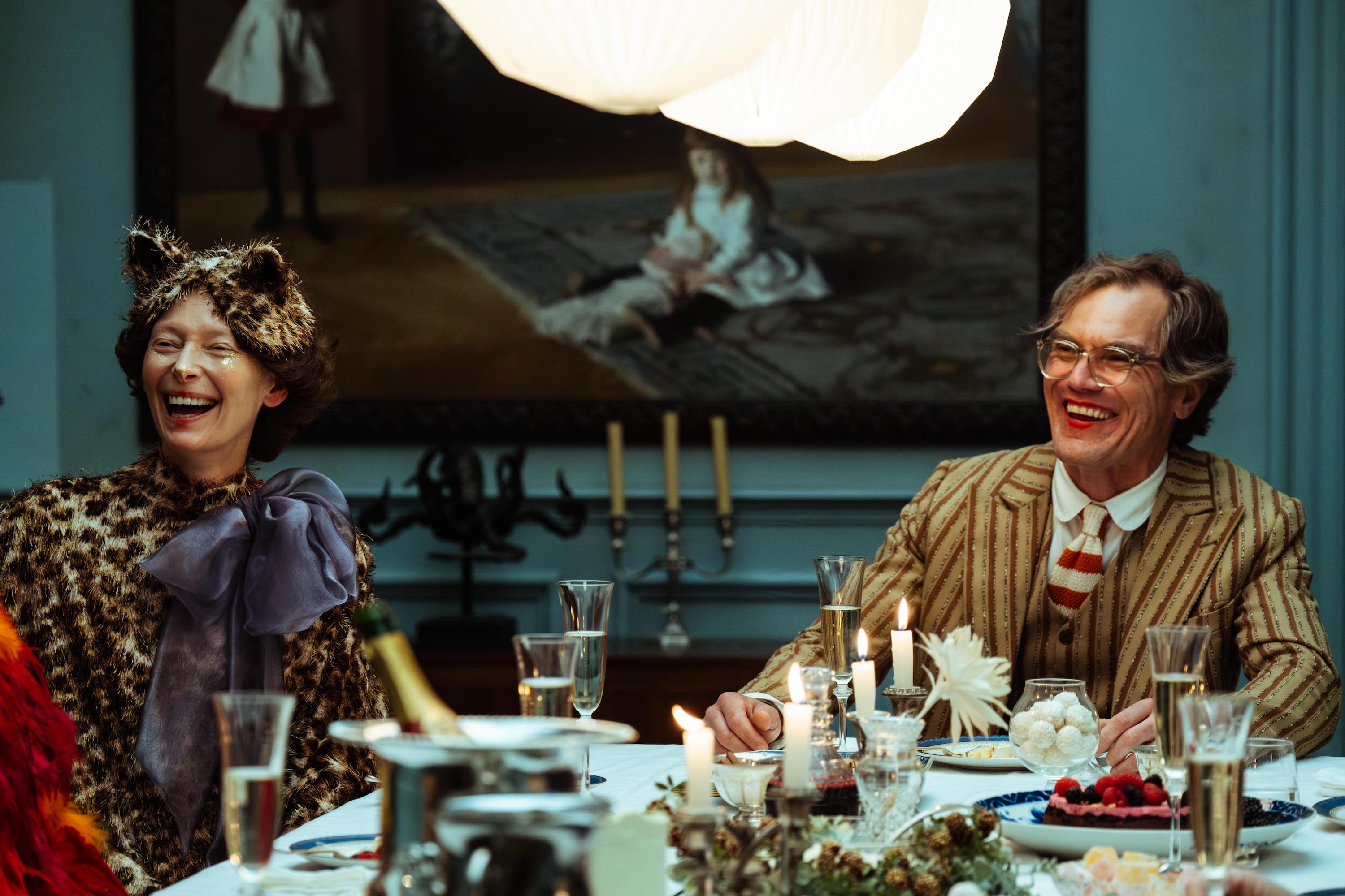 Tilda Swinton (in a leopard-skin cap complete with cat ears, and a leopard gown with an immense blue bow) and Michael Shannon (in a brown, vertically striped, wide-lapelled suit) sit together, laughing, at a lavishly laid table in The End