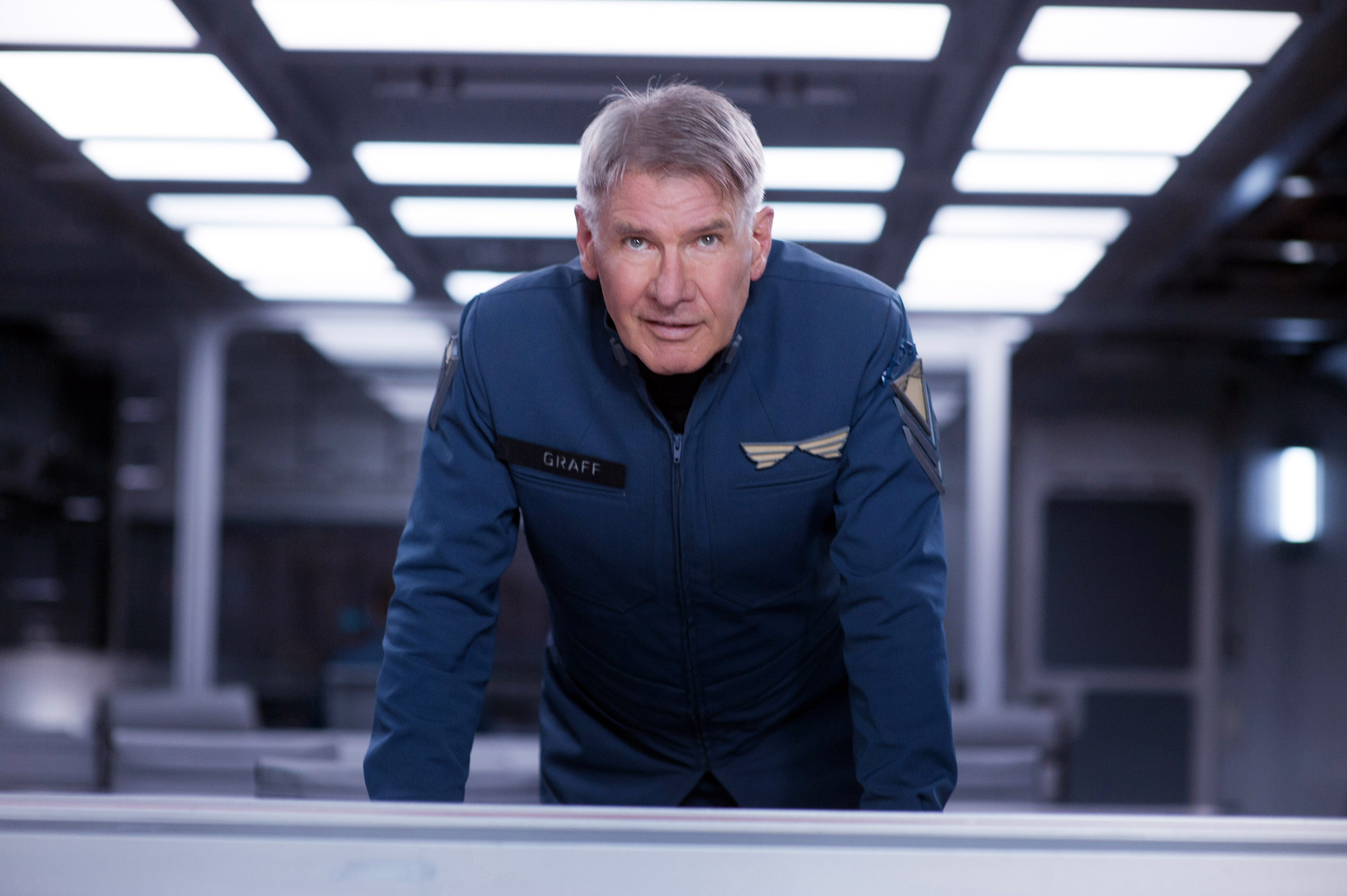 Harrison Ford in a futuristic space uniform leaning over a table in Ender’s Game