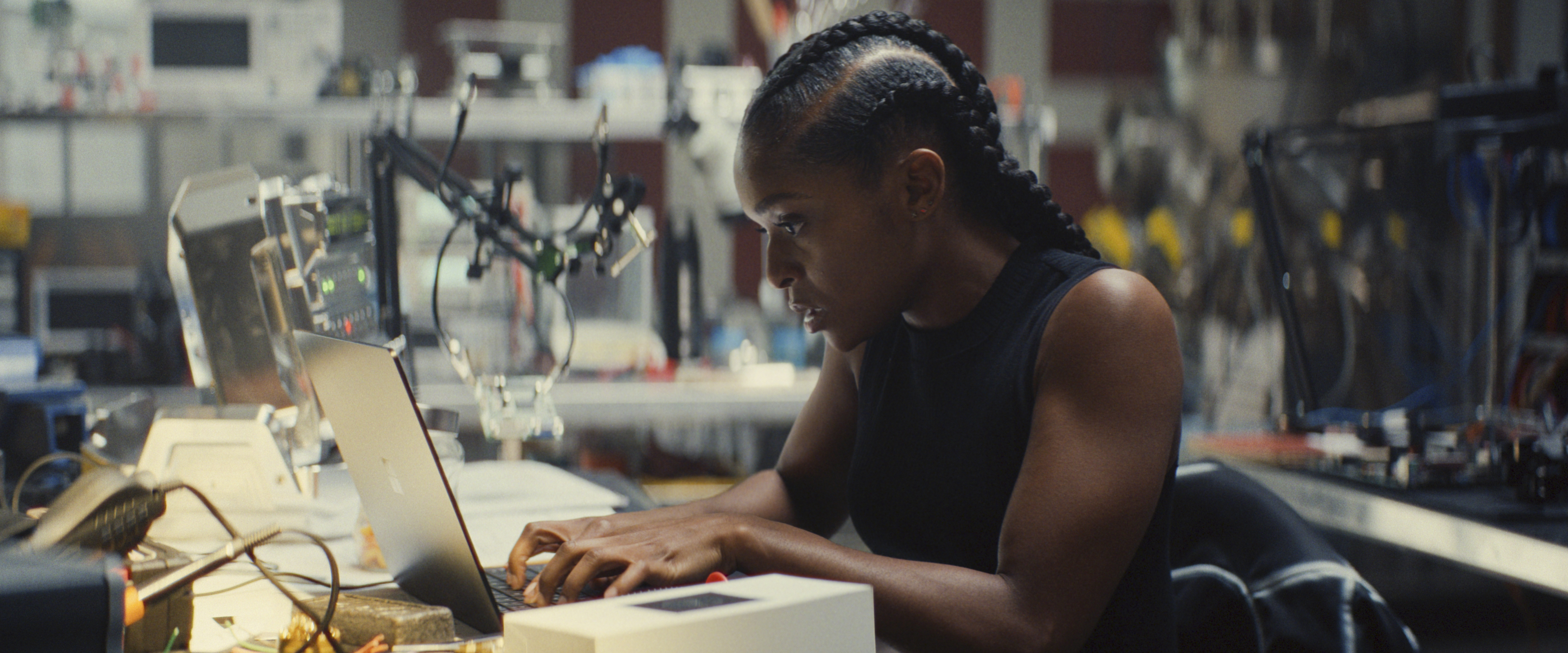 Dominique Thorne as Riri Williams works on a laptop in a robotics lab in Ironheart.