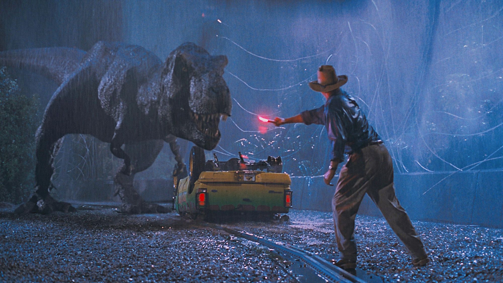 In an image from the 1993 film Jurassic Park, Alan Grant, played by Sam Neill, waves a flare at a T. rex to distract it from some imperiled children.