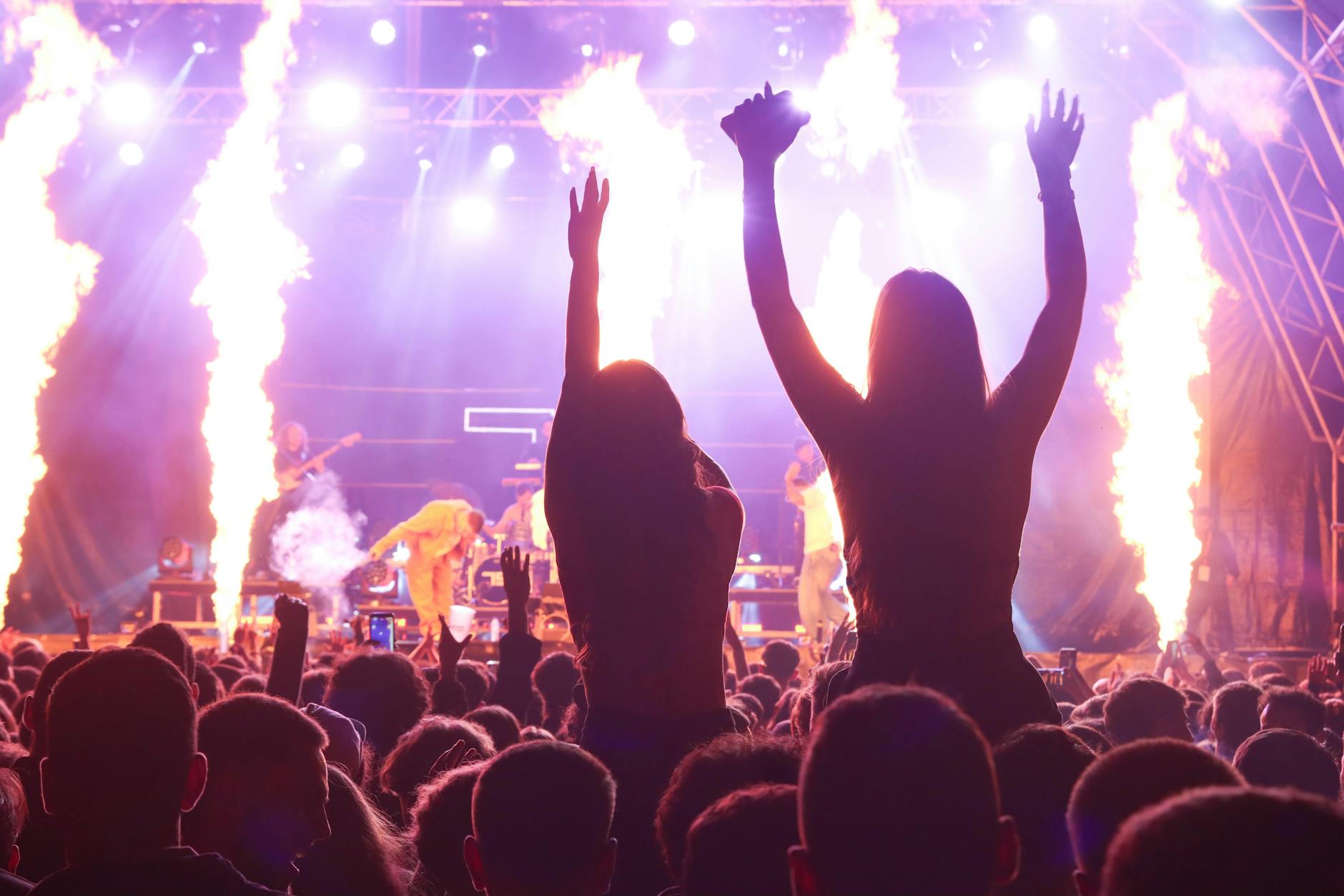 Large concert audience with raised hands and stage lighting creating energetic atmosphere