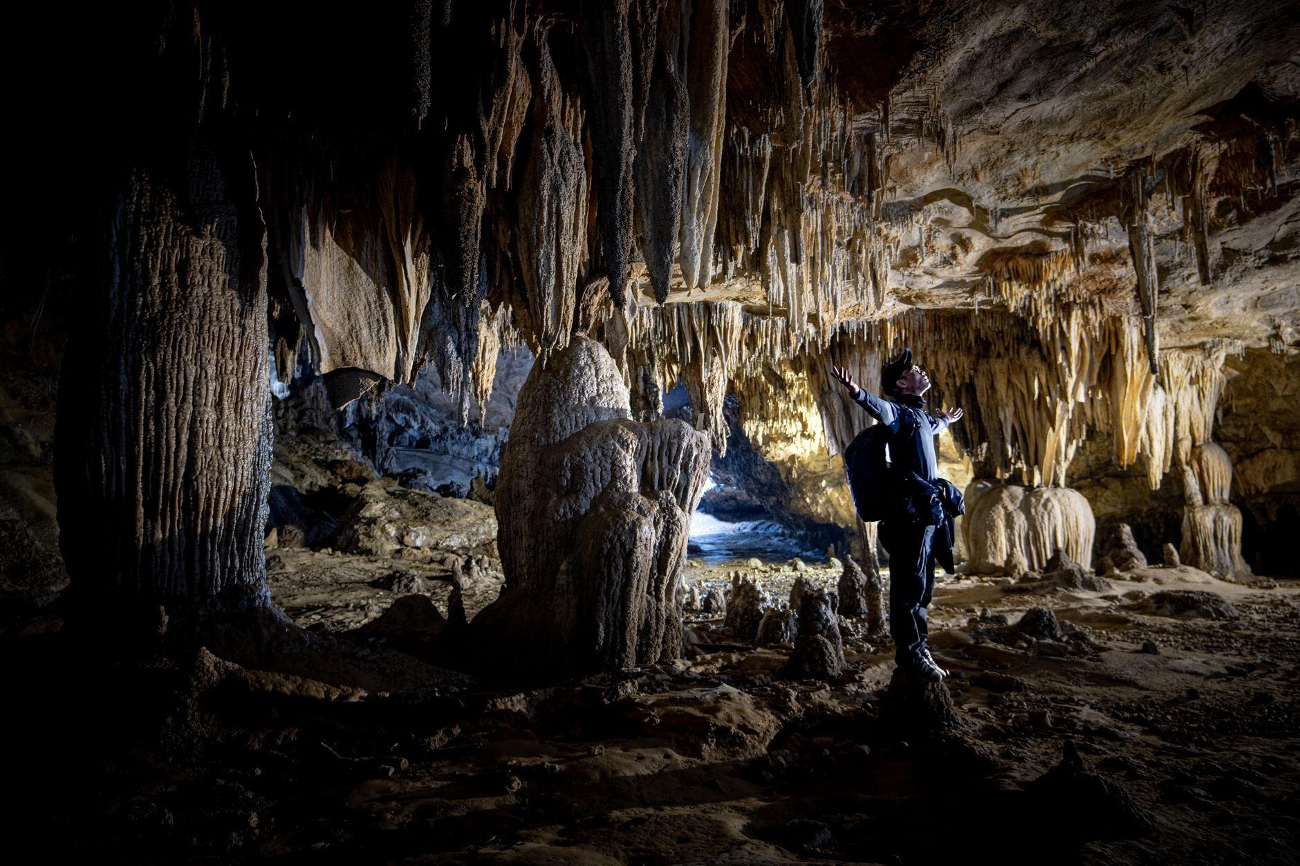Person exploring a dark underground cave environment lit by ambient light