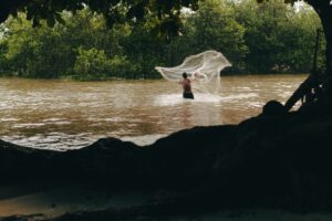 A person fishing along a tropical river bank surrounded by lush green foliage