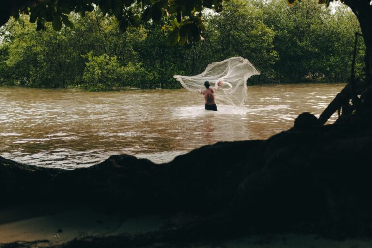 A person fishing along a tropical river bank surrounded by lush green foliage