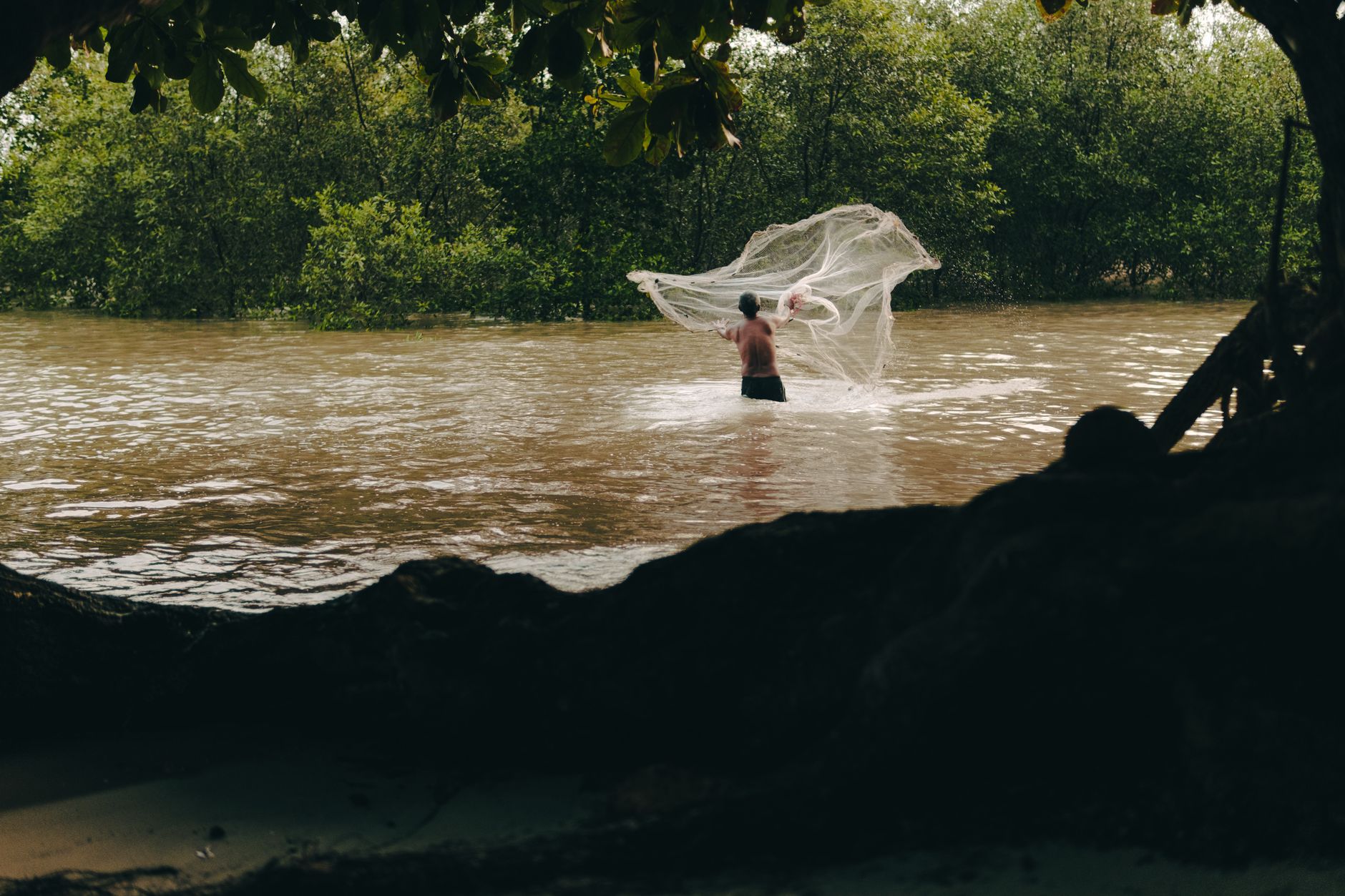 A person fishing along a tropical river bank surrounded by lush green foliage